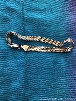 Full view of sterling silver serpentine style wide link bracelet laid out on blue fabric, showing overall design and length.