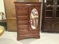 Front view of wood armoire showing eight drawers, four on the left and four smaller stacked on the right, with an oval mirror inset on the door.