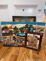 Photo showing three art pieces: colorful Ecuador village painting in background, abstract flower painting behind, and pressed flower framed art in front.