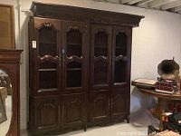 Full frontal view of the assembled three-piece dark wood cabinet showing upper chicken wire doors and lower solid wood doors with decorative molding and hardware.