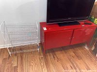 Photo showing the red metal cabinet and adjacent white metal wire shelf on wooden floor.