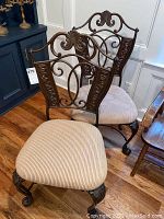 Two metal chairs with beige striped upholstered seats and ornate scroll metal backs, claw feet on legs.
