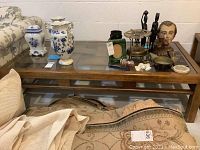 Full view of the wood coffee table with glass top, showing decorations on top (not included) and a folded rug beneath.