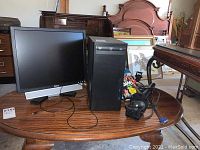 Overall view of Dell monitor, computer tower, monitor arm, and cables on wooden table.