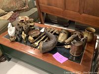 Wide view of table with brass pitchers, antique irons, spittoon and other brass/metal decorative pieces arranged