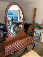 Full view of wood dresser top with large oval mirror and decorative carved base with 3 drawers.