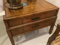 Front angled view of wooden end table showing two drawers with metal handles and surface scratches.