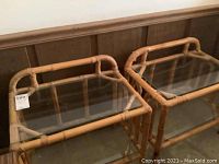 Two bamboo and glass end tables side by side against wood paneled wall