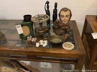 Full view of lot items on glass-top wooden table including brass burner, figurines, shell napkin rings, glass frame, small bowl, and dish.