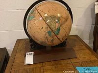 Side view of the antique globe on its metal and wooden stand placed on a wooden platform.