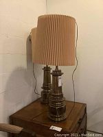 Pair of brass table lamps placed on a wooden surface against a white wall, showing overall design and size.