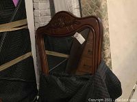 Large wood framed wall mirror with carved detail along the top, leaning upright against a mattress and covered partially by a moving blanket.