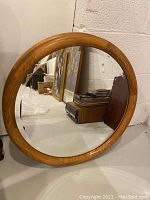 Photo of one round wooden mirror with beveled edge showing full mirror and frame.