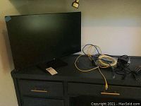 Front view of HP 27-inch monitor on a dresser with several cables beside it.