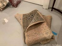 Partially folded beige and blue English Manor Karastan rug resting on floor showing pattern and edge detail