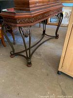 Photo showing the carved wood apron with detailed leaf and scroll designs and metal legs connecting to a curved metal stretcher base with claw feet.