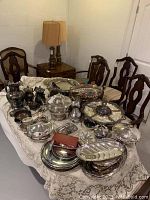 Wide view of table set with silver plate serving trays, bowls, coffee and punch sets, showing variety of items and arrangement.