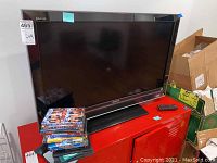 Front view of the Sony Bravia 40-inch TV showing the screen, remote on the side, and stack of DVDs on the TV stand.