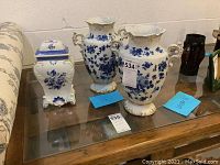 Front view of two porcelain vases and one jar with lid on glass surface showing overall set