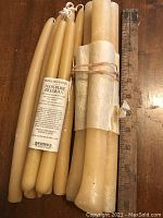 Photo showing all candles arranged on wood surface, taper candles on left labeled, thicker candles wrapped and tied on right next to a ruler for size.