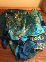 Photo showing the silk scarf loosely spread out displaying turquoise base color and cherry blossom design.