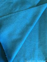Close-up photo showing the folded edges of the turquoise teal fabric, highlighting its texture and color.