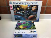 Two jigsaw puzzle boxes stacked, showing Ravensburger Universe 1000-piece puzzle and Art Gallery Underwater 500-piece puzzle