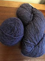 Two skeins of eggplant colored wool yarn from Briggs and Little with pale pink speckles, one wound and one in skein form, placed on a wooden surface.