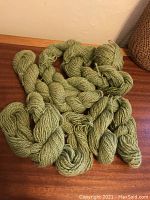 Six skeins of pale green wool yarn, mostly unwound, laid out on wooden surface.