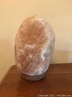 Front view of the Himalayan salt lamp showing salmon-colored salt rock on wooden base against beige background.