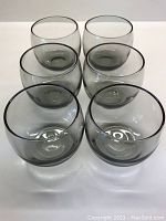 Set of six smoky grey, short, bulbous whiskey glasses viewed from above and front.