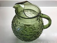 Full view of green textured glass pitcher showing shape, spout and handle.