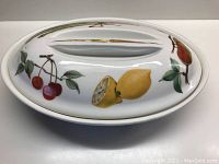 Top view of the oval porcelain casserole lid with painted fruits: cherries, lemon, and pear, featuring gold handle accents.