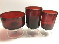 Close-up of three individual ruby red stemware pieces: dessert bowl with broad round base, wine/water glass, and shot glass, all with clear stems.