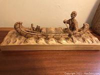 Side view of wood carving showing the man paddling the canoe on the water base