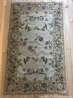 Full view of rectangular wool tapestry carpet showing floral design and border on light wooden floor.