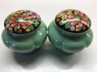Side view of the pair of vintage green ceramic salt and pepper shakers with colorful floral painted tops.