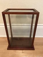 Front view of the wood and glass display case showing glass top and front panels inside wooden frame and fitted base.