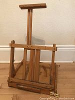 Front view of the wooden adjustable easel upright, showing brass locks, clips, and the easel frame