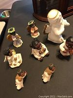 Photo showing seven out of eight angel figurines assembled on a black surface, including mix of resin and china materials.