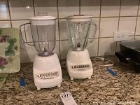 Two blenders side by side on kitchen counter: one Proctor Silex with plastic jar and one Hamilton Beach with glass jar