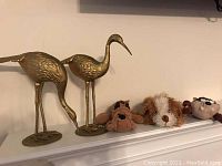 Pair of brass bird figurines next to three stuffed dog toys on a shelf