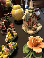 Photo showing seven decorative items including two glass flower baskets, ceramic rose, yellow candle, Christmas church music box, and Christmas-themed figurines
