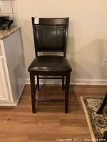 Front view of a single wood chair with black vinyl seat and backrest showing padded cushioning and wood frame.