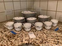 Wide view of the full collection showing cups in front and stacks of plates behind on granite counter