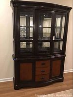 Front view of the two-piece china cabinet showing dark wood finish, three glass doors in the upper section, and two wooden doors with three central drawers in the lower section.