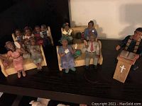 Five resin church figurines displayed on a shelf including preacher at lectern and four seated congregants in various attire and poses.