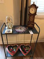 Full lot of five assorted clocks on black metal shelf: anniversary clock, decorative round clock with pink jewels, small decorative clock, and two heart-shaped clocks in ornate cases.