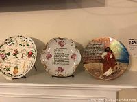 Three decorative plates displayed on stands on a mantle, showing overall view and designs