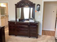 Front view of wooden dresser with mirror, showing nine drawers and faux marble top against wall.